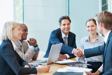 man shaking hands with another across a table with other sitting also