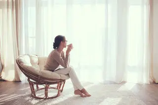 woman sitting in a chair sipping coffee while looking out the window