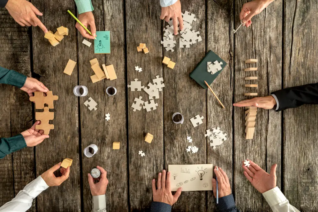 employees hands around a table showing puzzle pieces to show the importance of capabilities and skills in the workplace