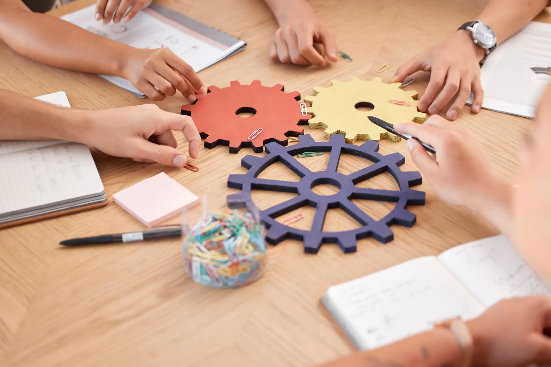 employee hands around a table putting gears together to work showing capabilities in the workplace